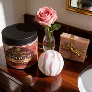 Body polish jar, bath bomb, and soap on a wooden surface with a rose.