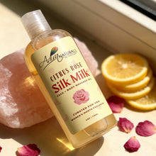 Bottle of Citrus Rose Silk Milk product by Adiva Naturals on a surface with pink stones, rose petals, and lemon slices.