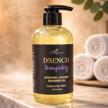 Bottle of Drench Tranquility shower oil on a bathroom counter with towels in the background