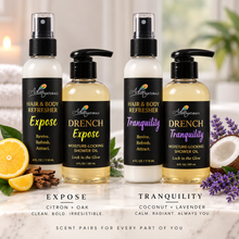 Four Adiva Naturals hair and body shower oil bottles displayed on a marble surface with decorative props including citrus, oat, lavender, and a coconut. The bottles are labeled Expose Refresher, Drench Expose, Tranquility Refresher and Drench Tranquility. Adiva Naturals Luxe Hair and Body Refreshers paired with DRENCH Shower Oils