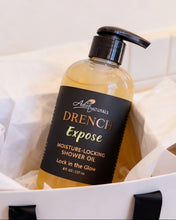 A bottle of Adiva Naturals Drench Expose shower oil with a black pump and black label, resting in white tissue paper inside a white gift box.