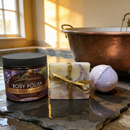 Adiva Naturals Lavender Bath products including a jar of 'Body Polish', a wrapped bar of soap, and a bath bomb on a stone surface with a copper bathtub in the background.