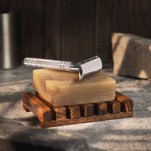 Shaving razor on a bar of soap with a wooden stand on a textured surface.